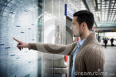 Young man traveling, reading train timetable in railway station Stock Photo