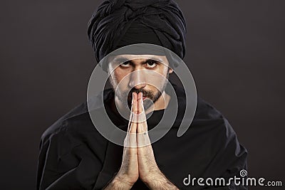 A young man in a turbanl prays with his hands folded in a petition in front of him. Close-up. Black background Stock Photo