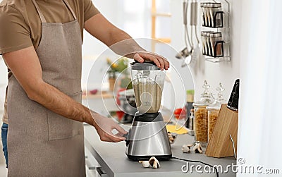 Young man using blender to cook cream soup in kitchen Stock Photo