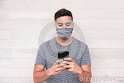 Young man using mobile phone app while wearing protective face mask during coronavirus outbreak - Millennial guy wathing videos on Stock Photo