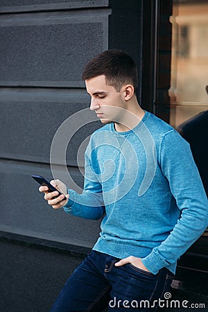 Young man is using the phone on the street. Handsome guy stand in front of window Stock Photo