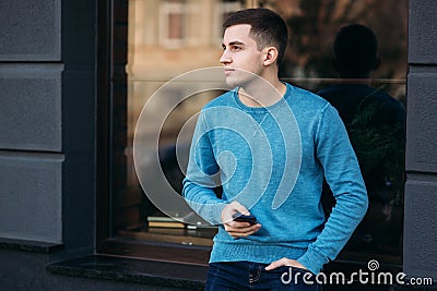 Young man is using the phone on the street. Handsome guy stand in front of window Stock Photo