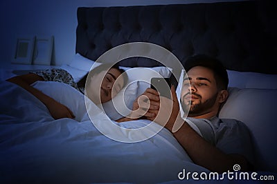 Young man using smartphone while his girlfriend sleeping in bed Stock Photo