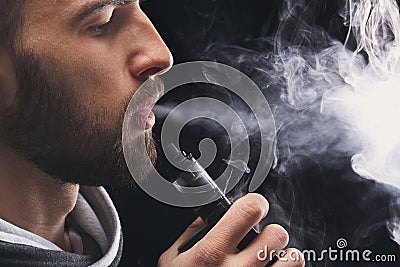 Young man vaping e-cigarette with smoke on black Stock Photo