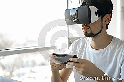 A young man vigorously plays a virtual reality video game wearing VR glasses. The man plays video games. Time relax. Stock Photo