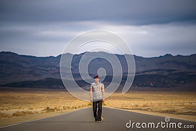 Young man walking alone through an empty street in the desert of Death Valley Stock Photo