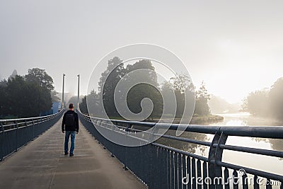 Young man walking on bridge over river Vltava in city Ceske Budejovice with fog Stock Photo