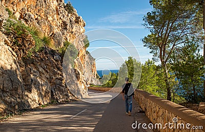 A young man walks on a mountain road traveling hitchhiking against the background of the sea Editorial Stock Photo