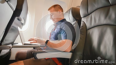 A young man was sitting on the plane and working on his laptop before departure. Stock Photo