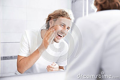 Young man washing face with soap near mirror Stock Photo