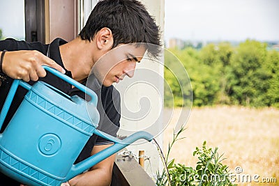 Young Man Watering Plants on Apartment Balcony Stock Photo