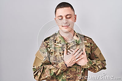 Young man wearing camouflage army uniform smiling with hands on chest with closed eyes and grateful gesture on face Stock Photo