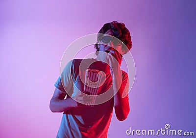 Young man wearing 3D glasses eating popcorn and watching exciting movie isolated on neon background Stock Photo