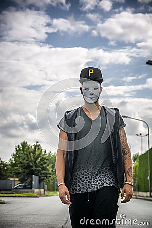 Young man wearing white creepy mask outdoor in city street Stock Photo