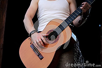 Young man, wearing white t-shirt and grey pants, playing guitar. Close-up picture of guitar in hands of musician singer, wearing Stock Photo