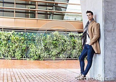 Young man wearing winter clothes in the street. Young guy with modern hairstyle with coat, blue jeans and white sweeter Stock Photo