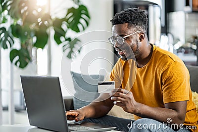 African-American young man wearing a yellow shirt making a purchase over the internet with a credit card Stock Photo