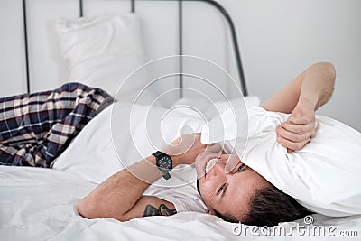 Young man in the white shirt lying on a bed with white linen and covers his head with a pollow Stock Photo