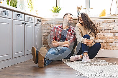 Young man and woman sitting on floor in kitchen and talking. Loving young couple spending time together at home Stock Photo