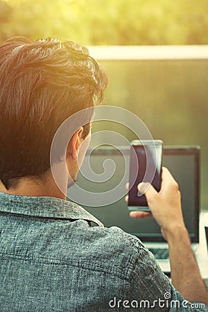 Young man working from terrace with smartphone and laptop Stock Photo