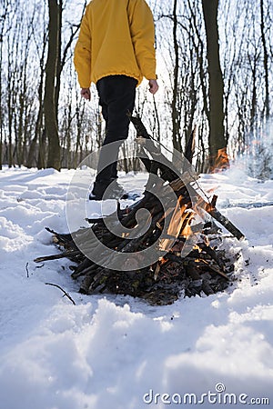 Young man in yellow jacket in the winter forest standing near small fire. Stock Photo