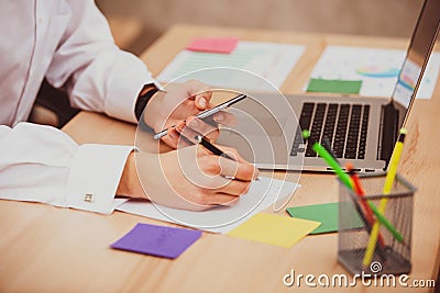 Young manager man using mobile phone in office and makes notes on paper sticker . Close-up hands, table, laptop Stock Photo