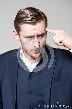 Young businessman pressing his pointing finger over forehead Bright mind dealing with problem. Bearded blond man Stock Photo
