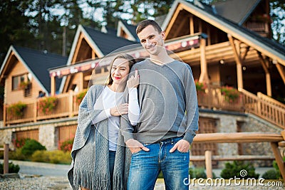 Young married couple standing outside their large wooden cottage in the woods. Stock Photo