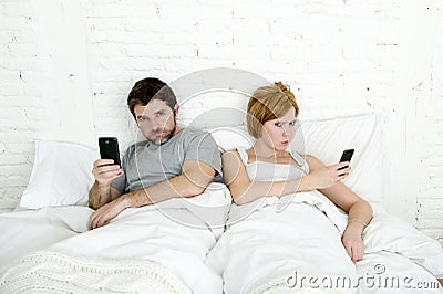 young married couple using their mobile phone in bed ignoring each other in relationship communication problems Stock Photo