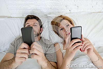 young married couple using their mobile phone in bed ignoring each other in relationship communication problems Stock Photo