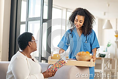 Young medical attendant bringing some food for elderly lady Stock Photo