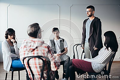 Young man admitting that he is an alcoholic during support group meeting Stock Photo