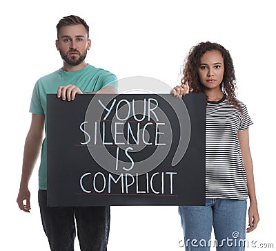 Young man and African American woman holding sign with phrase Your Silence Is Complicit on white background. Racism concept Stock Photo