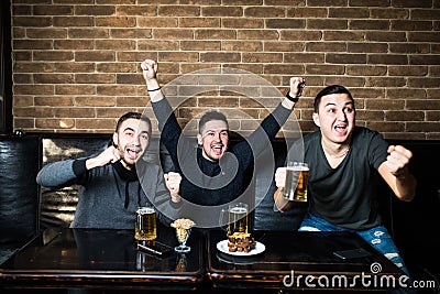 Young men drink beer, eat snaks and cheering for football match. Winning emotions. Stock Photo