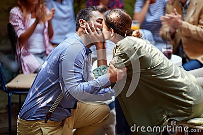 A young man kissing his girlfriend after asking to marry him at a party in a bar with friends. Leisure, bar, love, outdoor Stock Photo