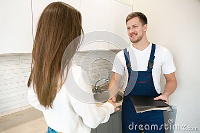 Young man plumber and brunette woman client shaking hands after successful work on water tap installation professional Stock Photo