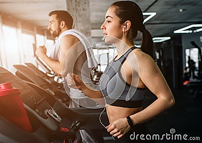 Young man and woman are running on the running machine. They do this exercise every time they come to fitness club.Close Stock Photo