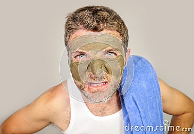 Young messy funny man looking at himself horrified in bathroom mirror with green cream on his face applying beauty facial mask pro Stock Photo