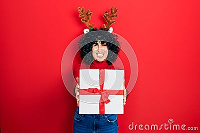 Young middle east woman wearing deer christmas hat holding gift smiling and laughing hard out loud because funny crazy joke Stock Photo