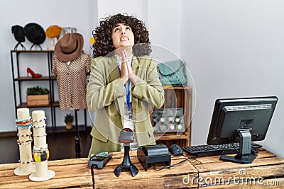 Young middle eastern woman working as manager at retail boutique begging and praying with hands together with hope expression on Stock Photo