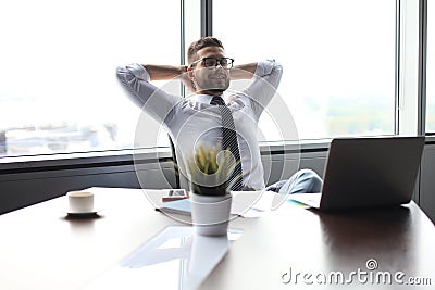 Young modern business man keeping hands behind head and smiling while sitting in the office Stock Photo