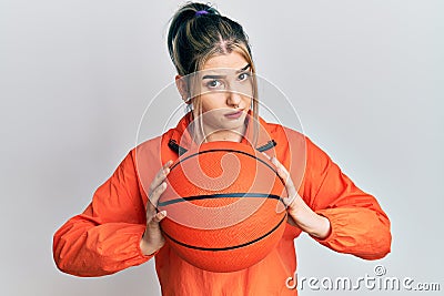 Young modern girl holding basketball ball skeptic and nervous, frowning upset because of problem Stock Photo