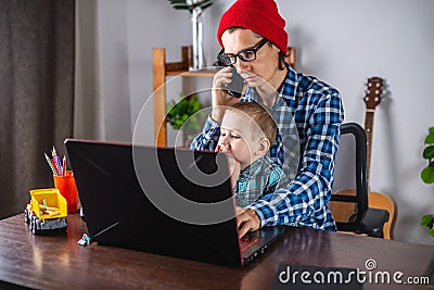 Modern man is working on a laptop, and his little son is sitting on his lap. Concept of family and remote work from home Stock Photo