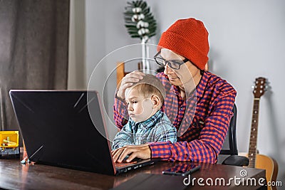 Modern man is working on a laptop, and his little son is sitting on his lap. Concept of family and remote work from home Stock Photo