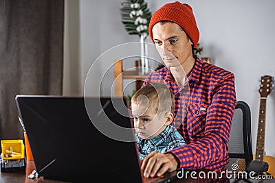 Modern man is working on a laptop, and his little son is sitting on his lap. Concept of family and remote work from home Stock Photo