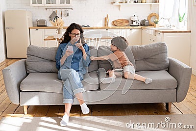 Young mom or babysitter use smartphone ask kid to keep quit. Child disturb mother from mobile phone Stock Photo