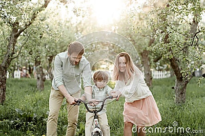 Young mom and dad teach their son to ride a bike Stock Photo