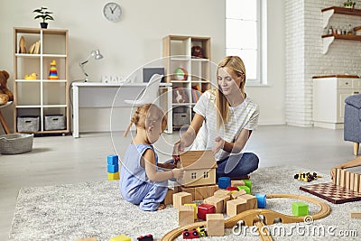 Young mom playing with cute little son and teaching him to build toy house in cozy modern apartment Stock Photo