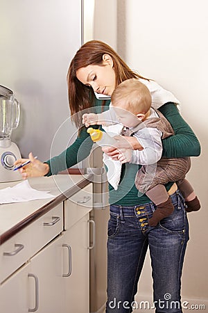 Being a mom is a real juggling act. Young mom trying to multi-task while holding her baby son and his bottle. Stock Photo