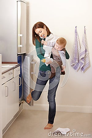 Being mom is a balancing act. Young mom trying to multi-task on the telephone while holding her baby son. Stock Photo